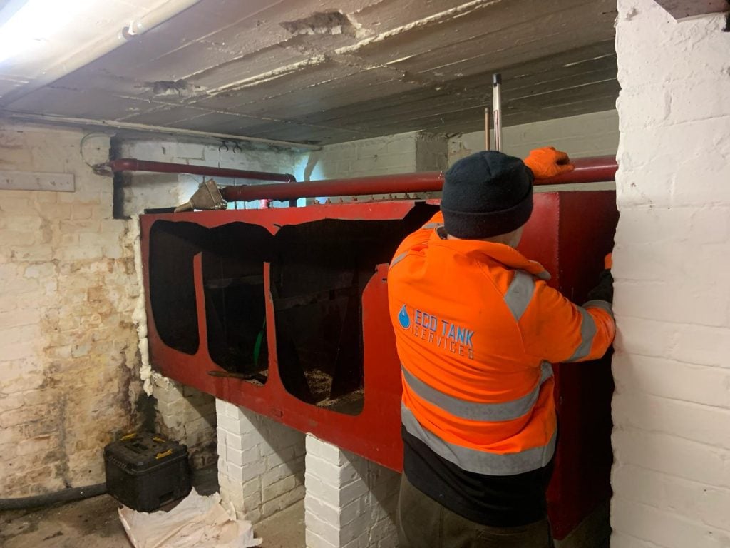 Eco tank Services engineer removing a metal oil tank from a basement area.