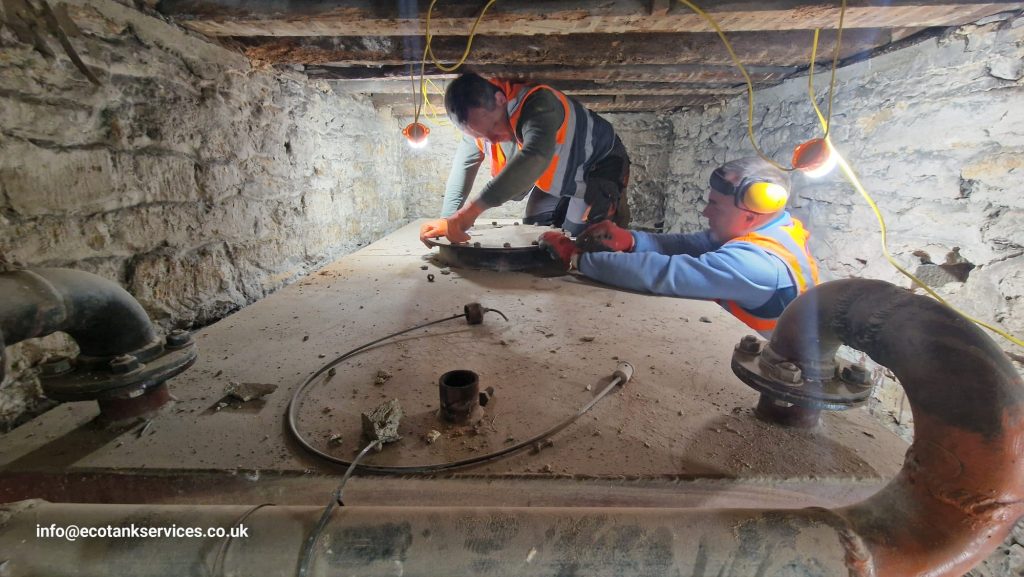 Engineers cleaning a 5000-litre metal oil tank in a basement environment.