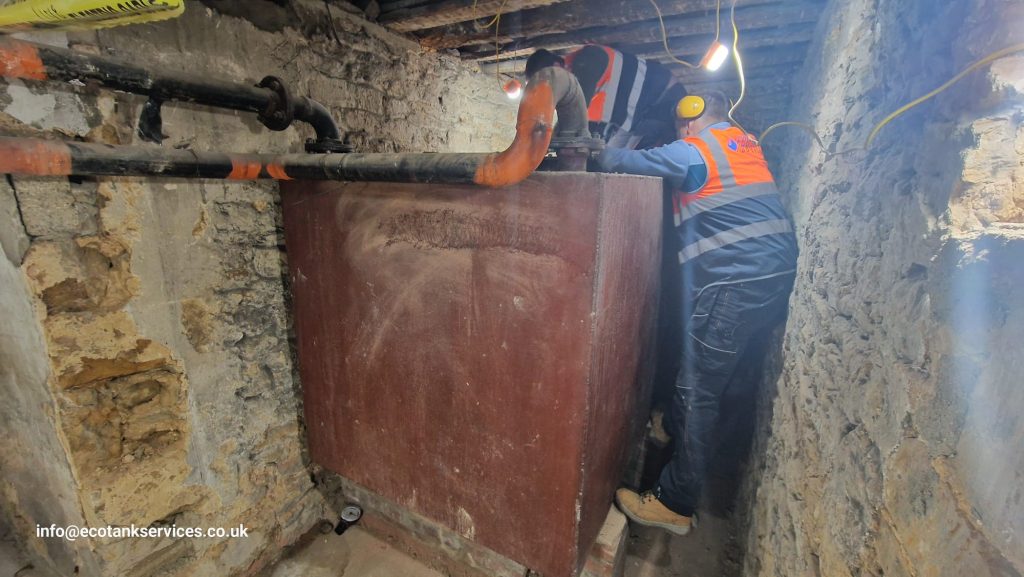 Engineers cleaning a 5000-litre metal oil tank in a basement environment.