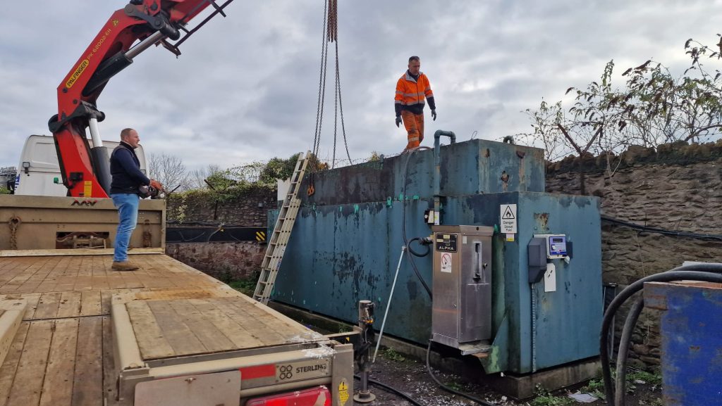 Workers performing commercial metal tank decommissioning with heavy equipment on site.